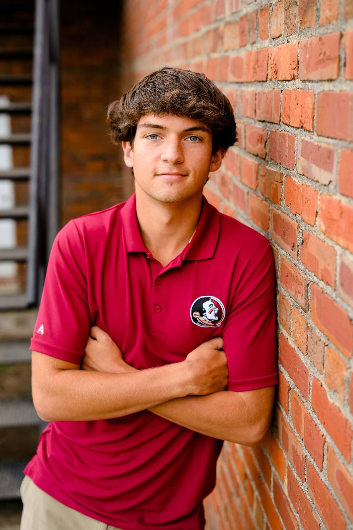 high school senior wearing a florida state shirt leans against a brick wall