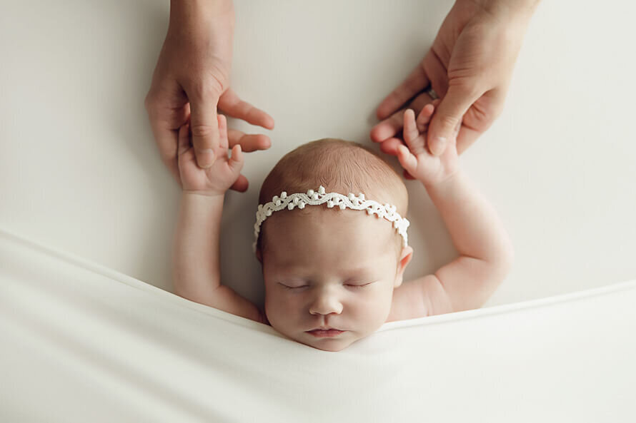 Baby sleeps during her photoshoot while her parents holds her hands over her head.