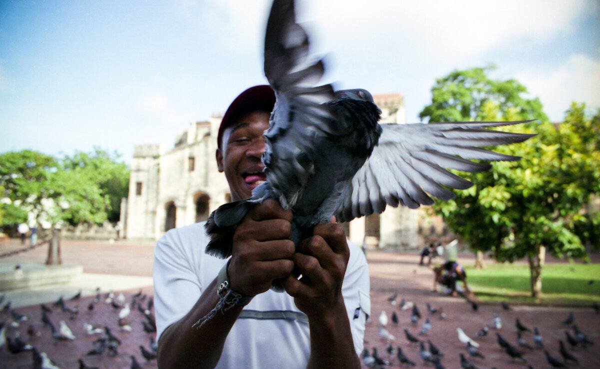 A man grabs the feet of a pigeon in front of the Basilica Cathedral of Santa María la Menor