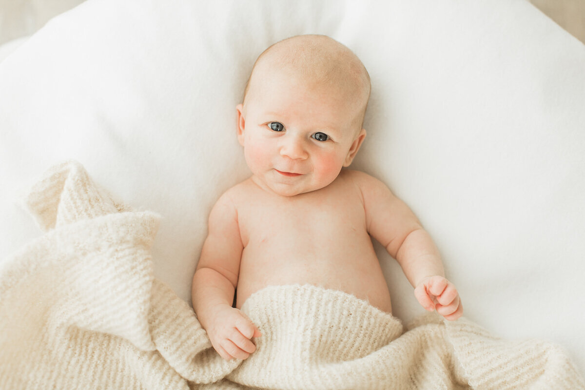 Newborn baby lays in white blankets and smiles and camera