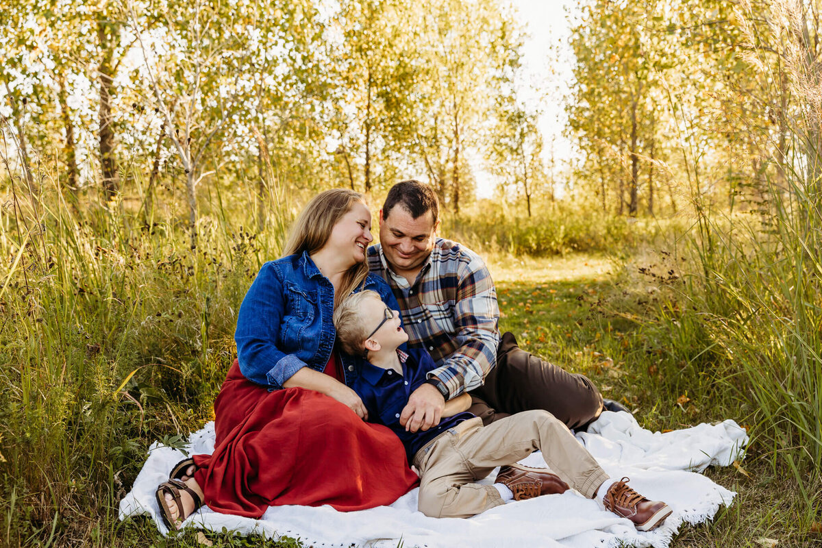 Mother, father and son snuggled on a white blanket laughing with each other during family photos.