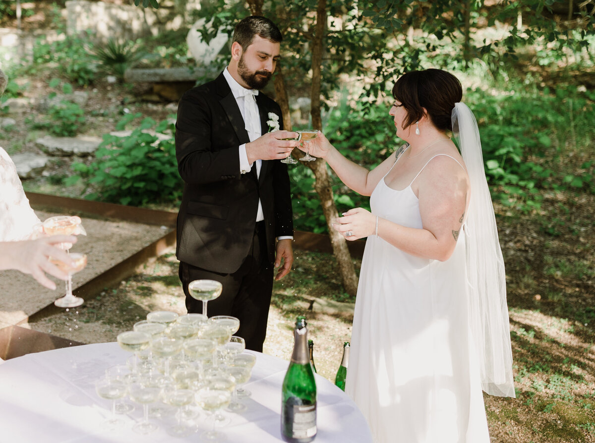 Bride and groom toasting glasses at Umlauf Sculpture Garden, Austin