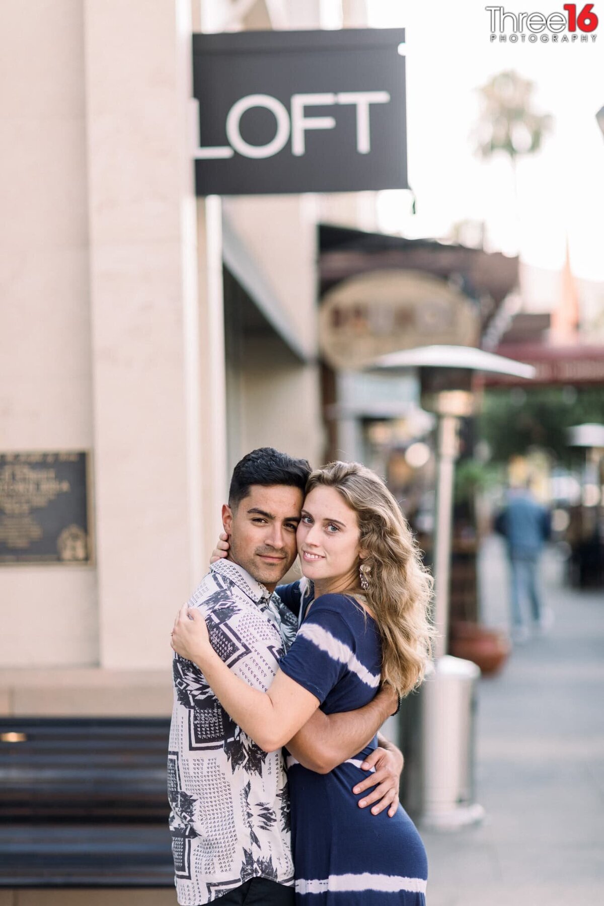 Engaged couple fully embrace each other as they look towards the engagement photographer