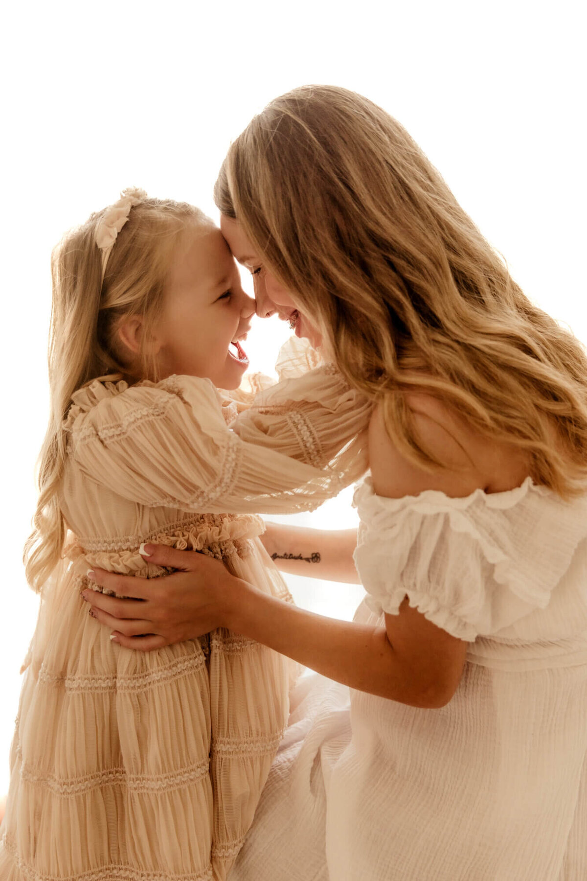Young girl laughs while touching noses with her pregnant mother.