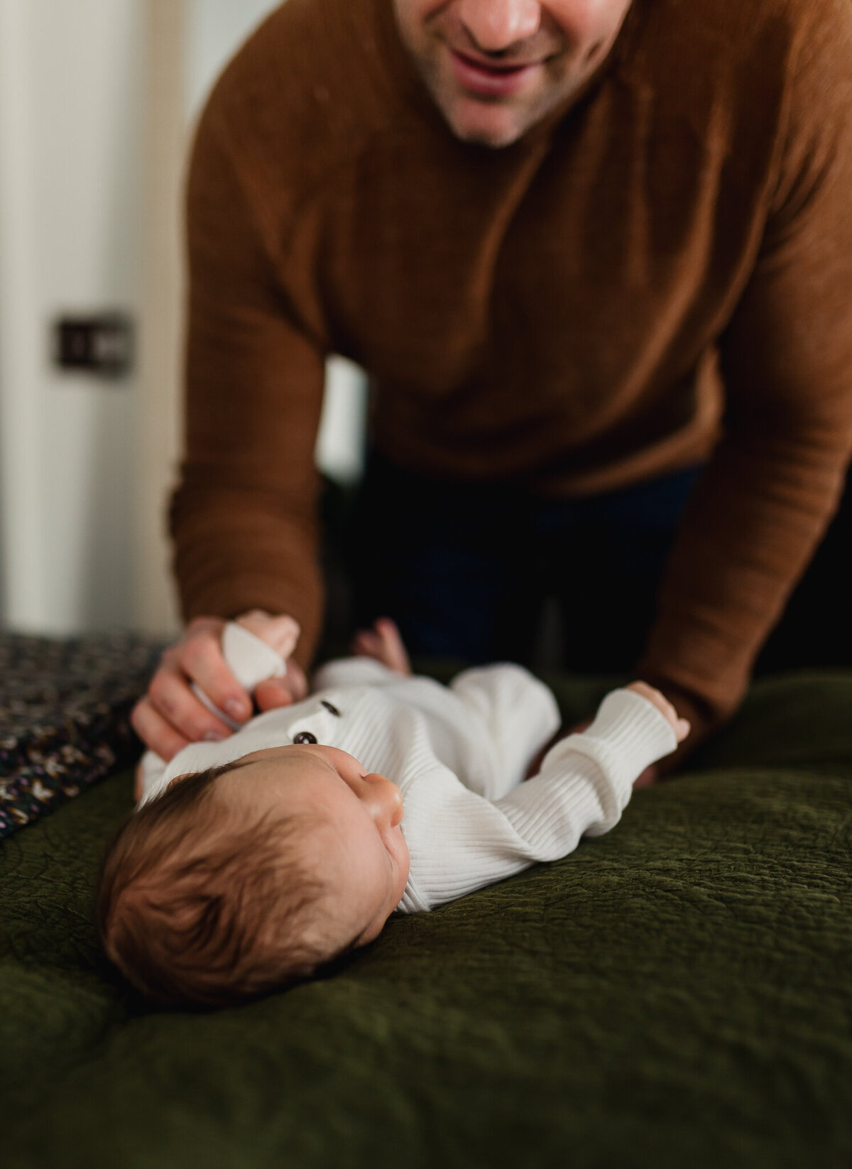 Baby laying on a bed with dad playing with hand.