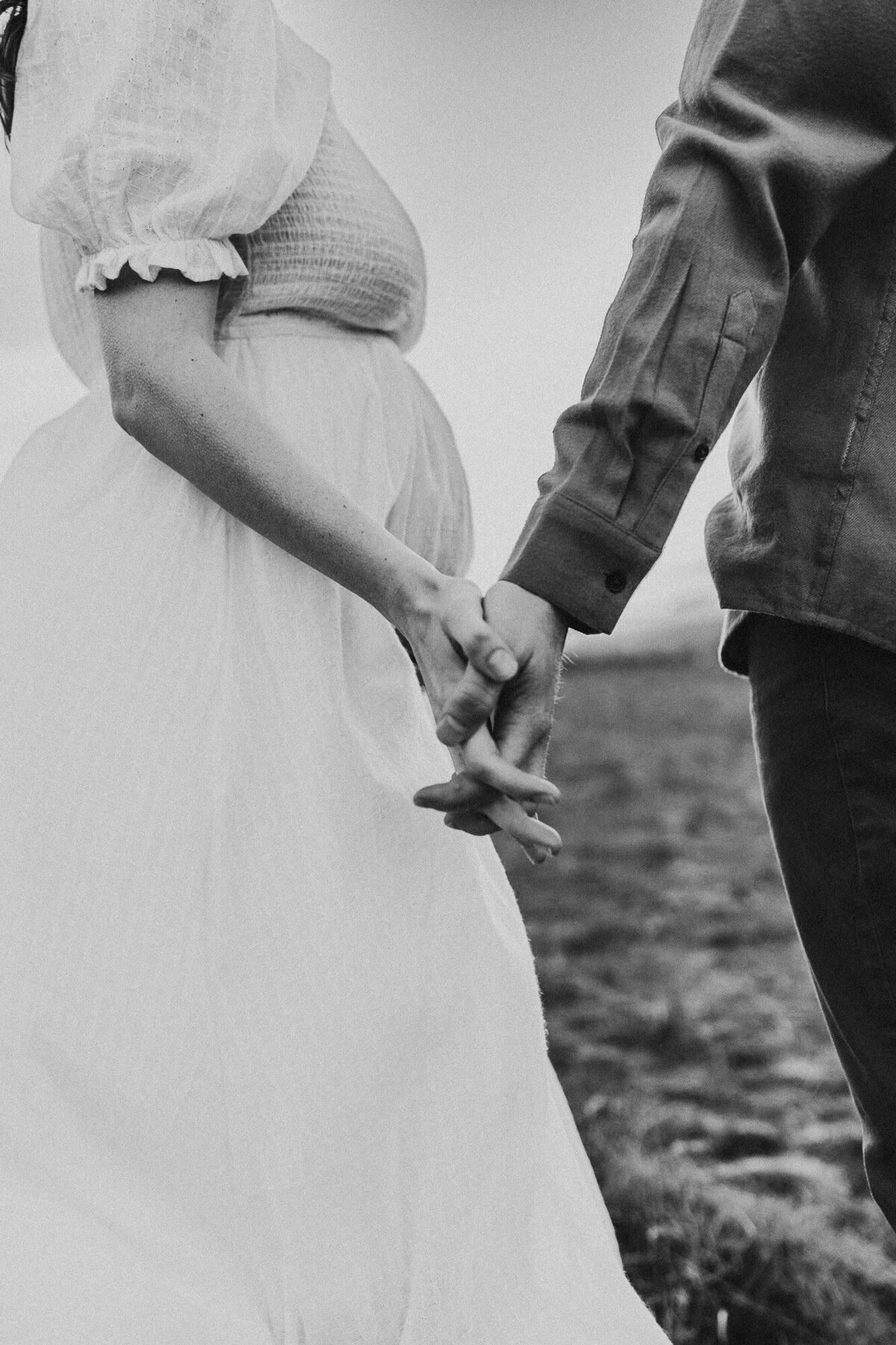 Monochrome image of couples hands holding and pregnant belly.