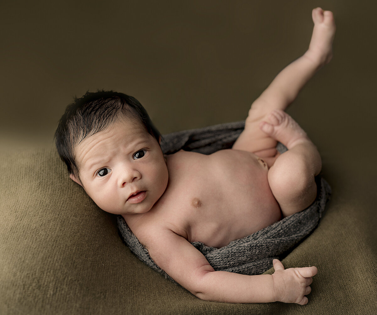 baby wrapped in grey wrap on green backdrop