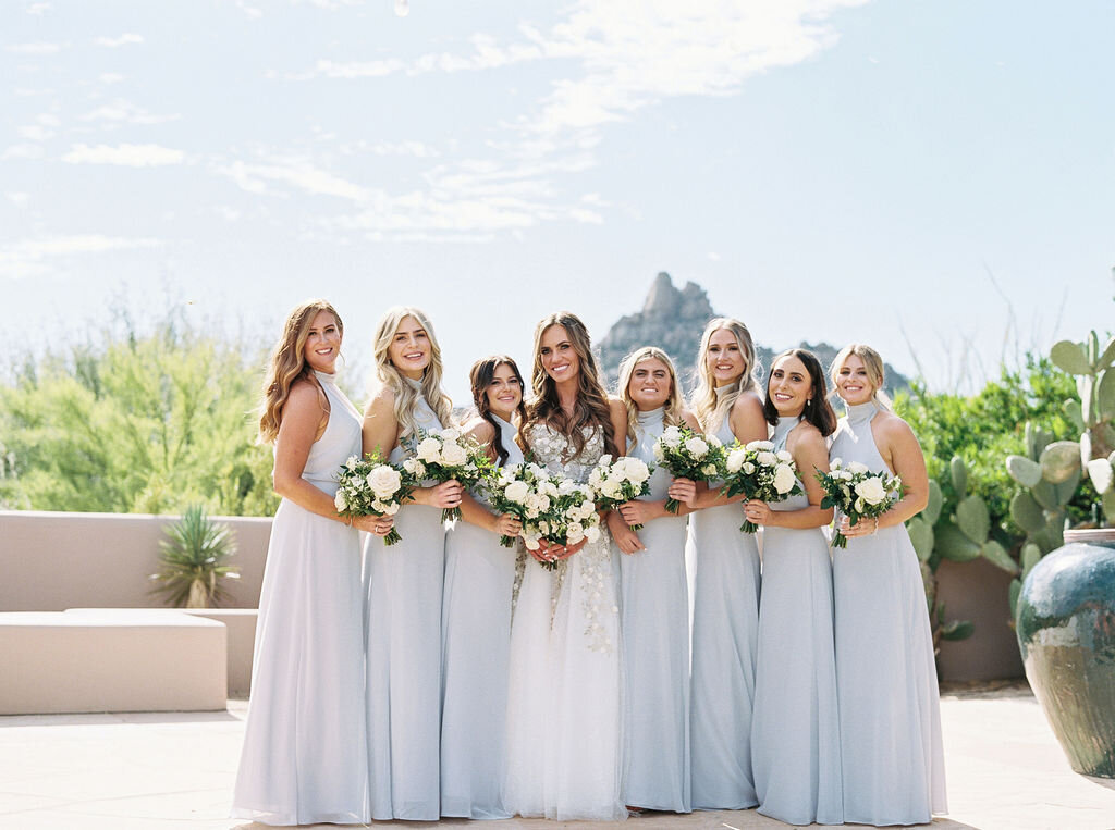 A stunning outdoor wedding photo featuring the bride with her bridesmaids in elegant soft blue dresses, holding white floral bouquets. Perfect wedding inspiration for bridesmaids' attire.