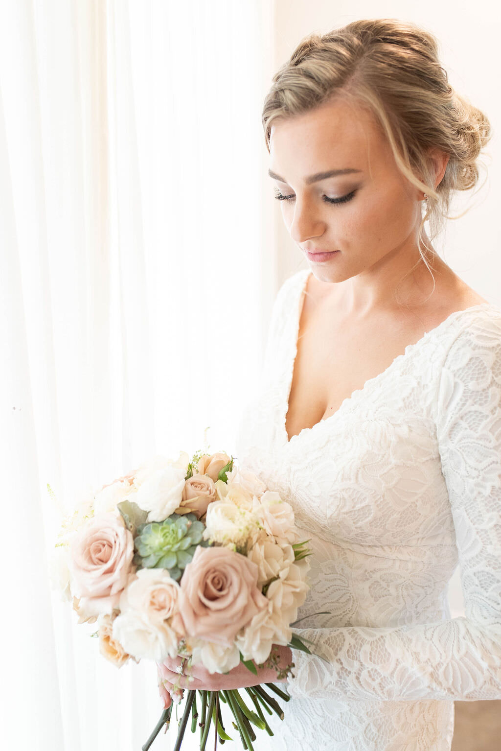 A bride looking down at a bouquet in her hands.