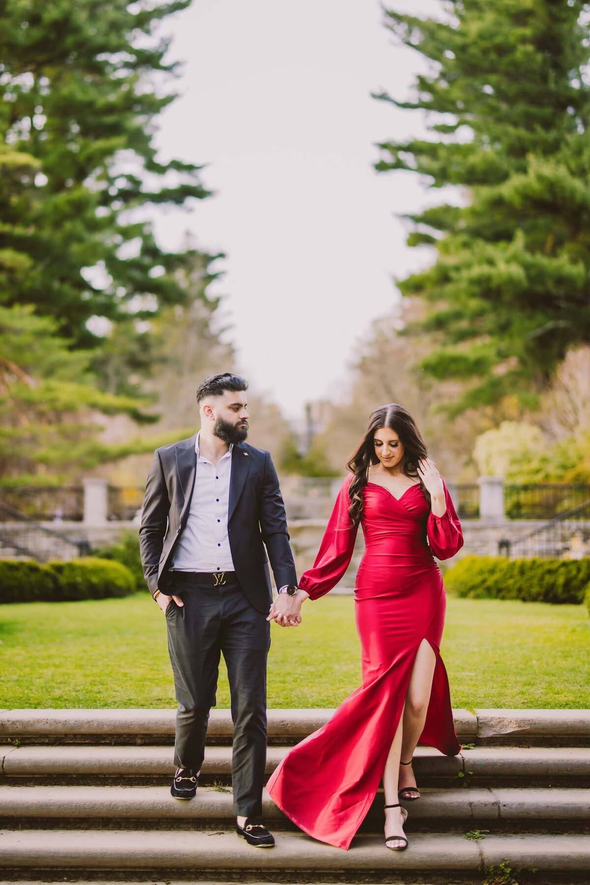 An engaged couple in red formal clothing walking down the steps at the nj botanical garden in ringwood state park