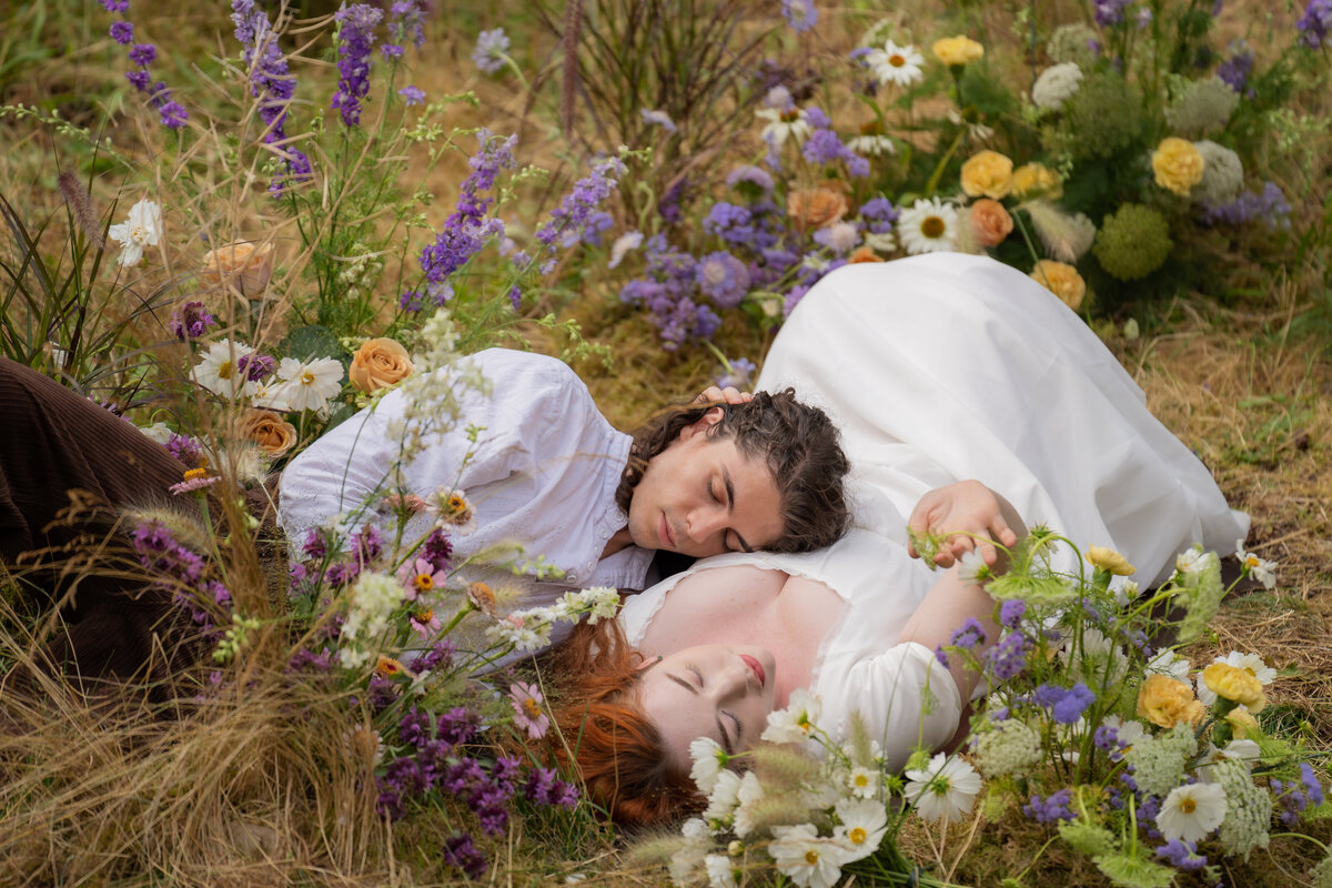 A couple laying together in the grass surrounded by flowers