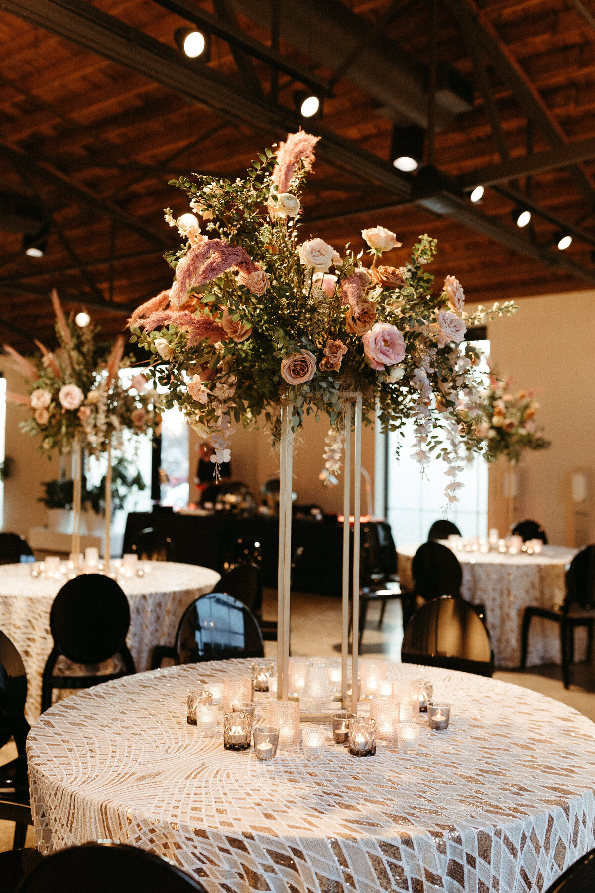 Stunning elevated centerpieces decorate this art deco wedding. Floral hues of terra cotta, mauve, burgundy, and dusty pink are brought to life with petal heavy roses, dried branches, and pink pampas grass. Designed by Rosemary and Finch in Nashville,