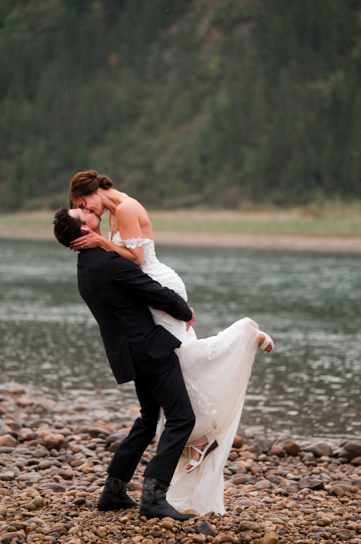 groom lifts his bride into a romantic kiss along the river in Edmonton, Alberta