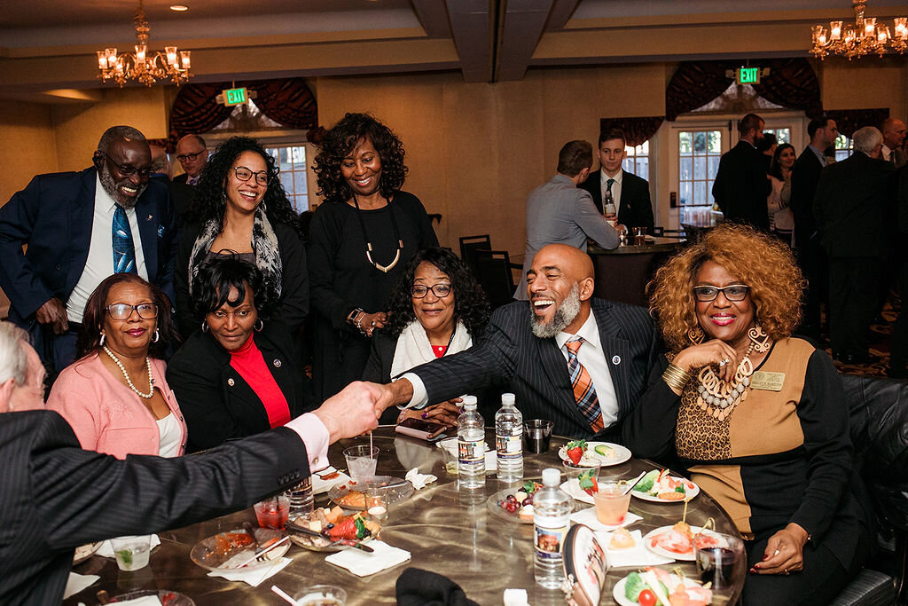 People sit around a table with food, while two people shake hands.