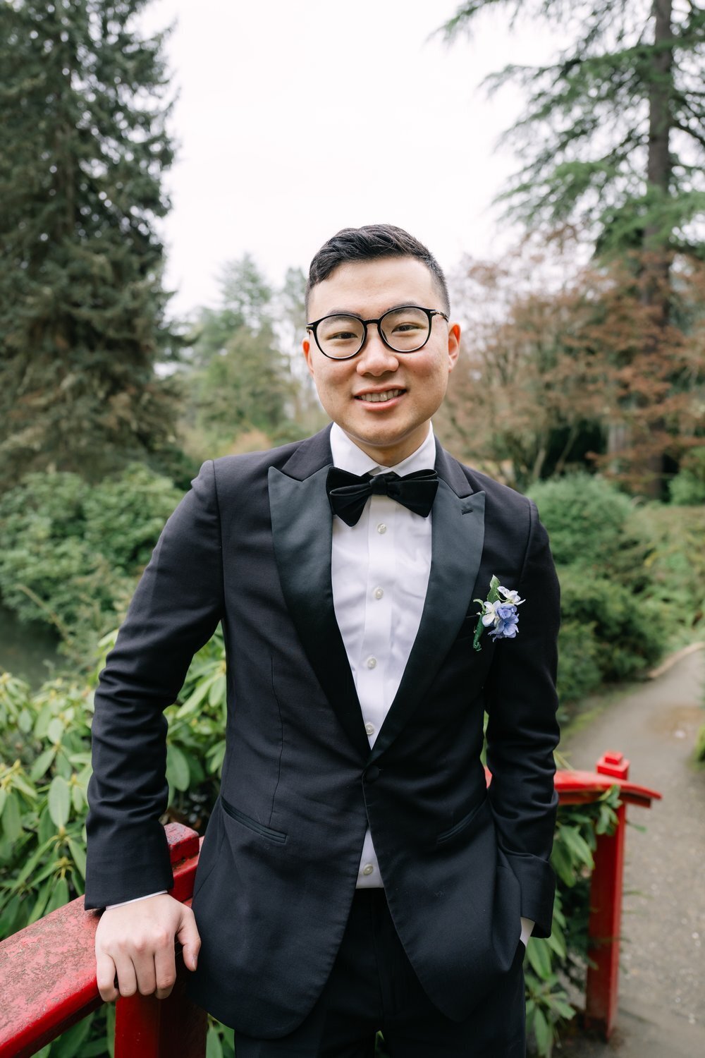 groom poses on red bridge at garden in seattle