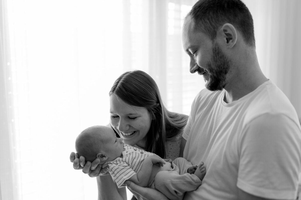 Schwarz weiß Bild von Mann und Frau. Er hält ein Baby im Arm, die Frau lächelt es an