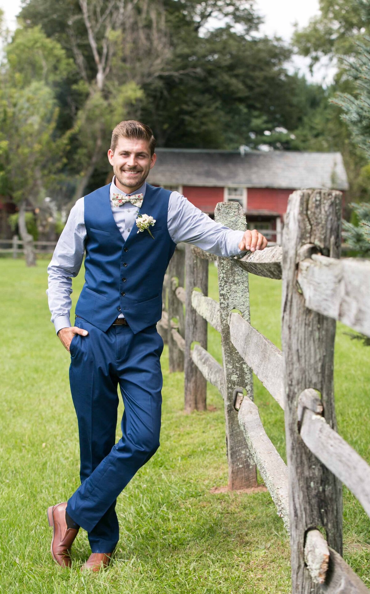 Groom, standing next to wooden fence wearing a navy suite with brown leather shoes.  Private Estate New Hope Pennsylvania