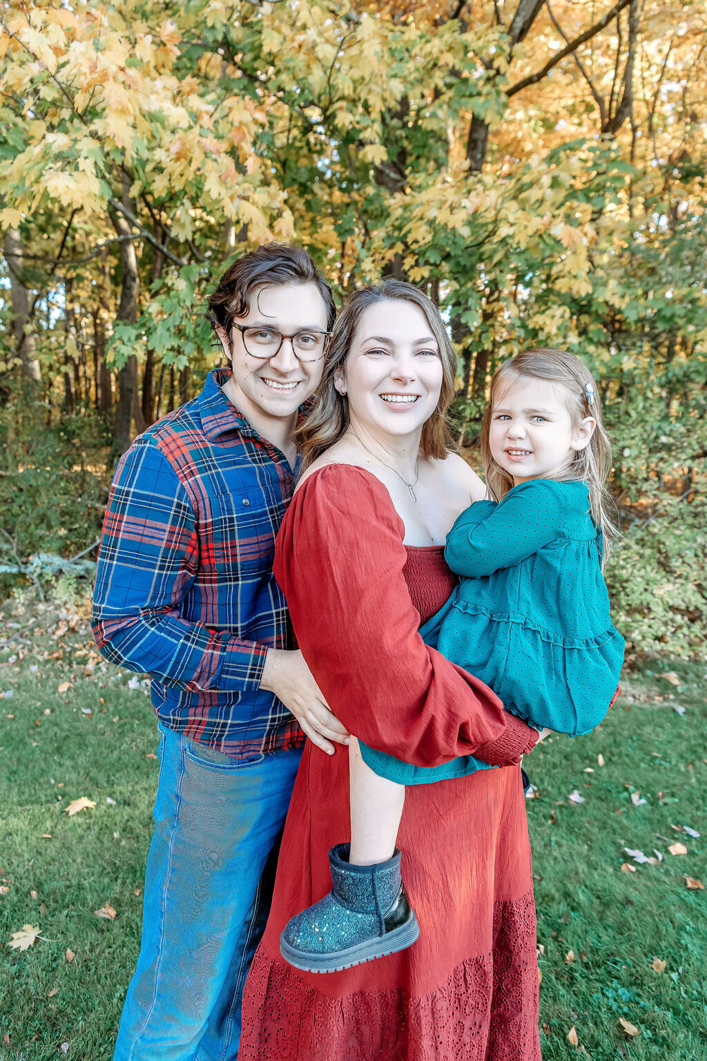 Connecticut family photographer captures happy family of three embracing in coordinated plaid and red outfits during fall session