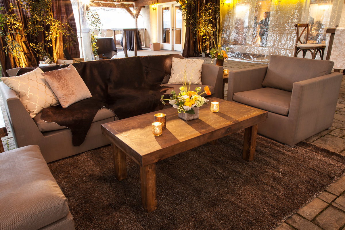 corporate party at Chateau Lill tent with ceiling greenery, lounge furniture, and yellow flowers, and brown draping, with wooden tables