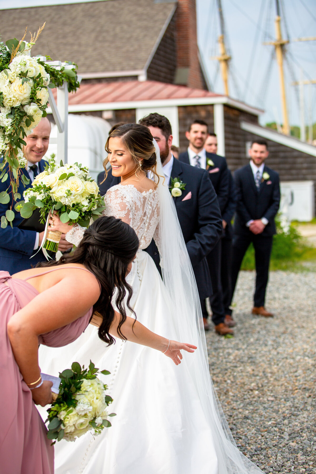 Bride hands her bouquet to her maid of honor during a wedding ceremony at the Mystic Seaport.