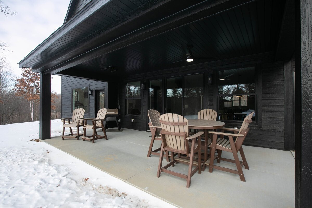 Exterior back view of custom home in Elk River, Minnesota with black siding, wood details and patio built by Cornerstone Custom Builds