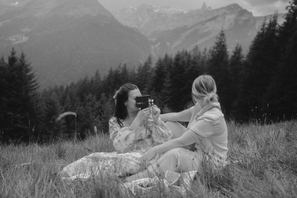 same sex couple at their switzerland elopement, sitting in the grasses using a film camera