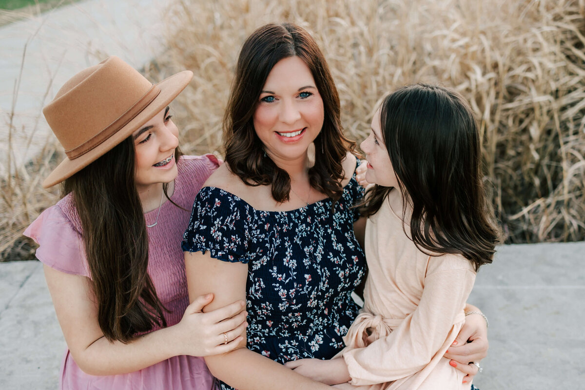 a mother and her two daughters sitting  together, the girls are looking at their mom and the mom is looking at the camera