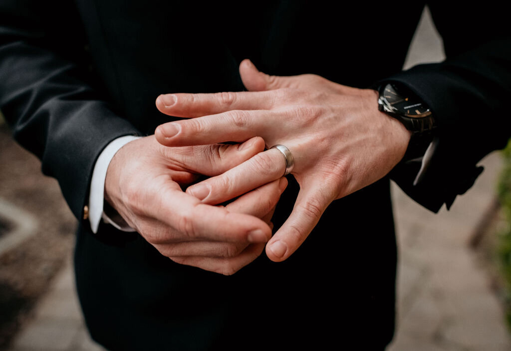 Detail shot of the groom's hand with his wedding ring at the Palm Event Center in Pleasanton, CA. The spring wedding features a sophisticated color scheme of gold, black, and white, highlighting the elegant ring and stylish attire.