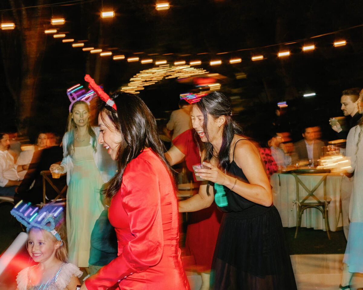A joyful party scene with people dancing and laughing. Guests wear festive light-up headbands, surrounded by string lights.