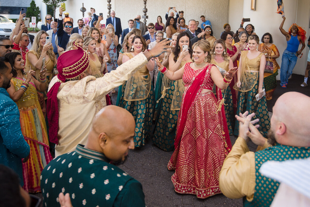 Vibrant Indian wedding baraat celebration at Le Méridien Charlotte. The bride and guests in colorful lehengas and sarees dance joyfully with the groom’s family during the outdoor procession. Captured by a Charlotte Indian wedding photographer specializing in candid, cultural wedding moments full of tradition and energy.