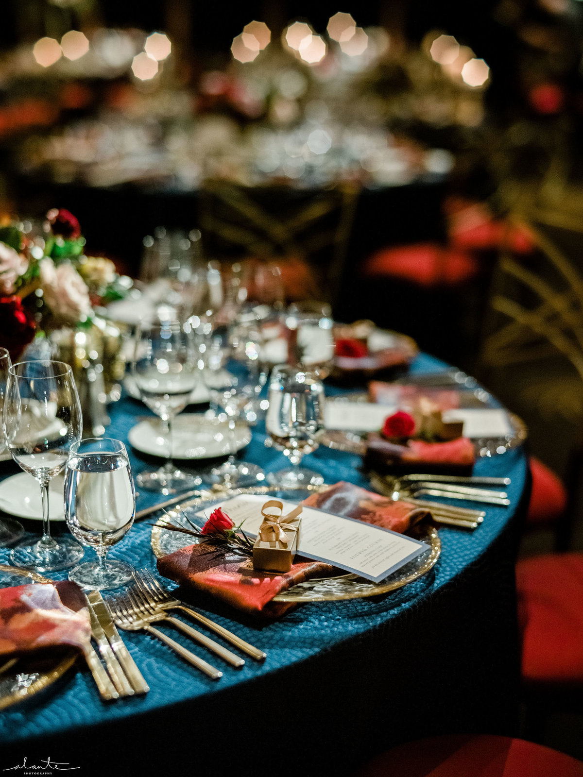 round wedding reception table with nav blue linen, red and pink napkins, and gold rimmed glass charger plates