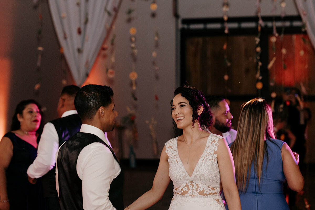 The bride and groom enjoy dancing with their guests, with whimsical decorations hanging from above, creating a festive atmosphere.