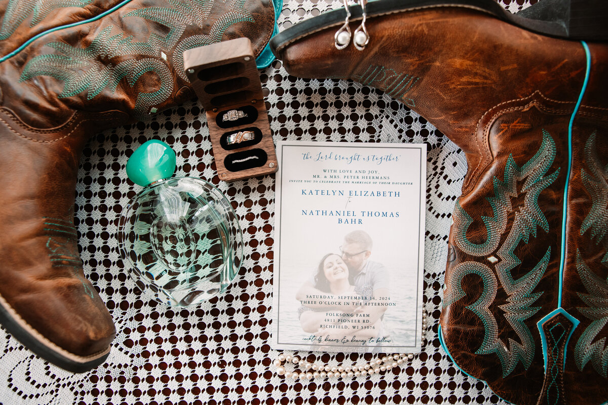 A bride's jewelry, boots and perfume sit together on a tablecloth