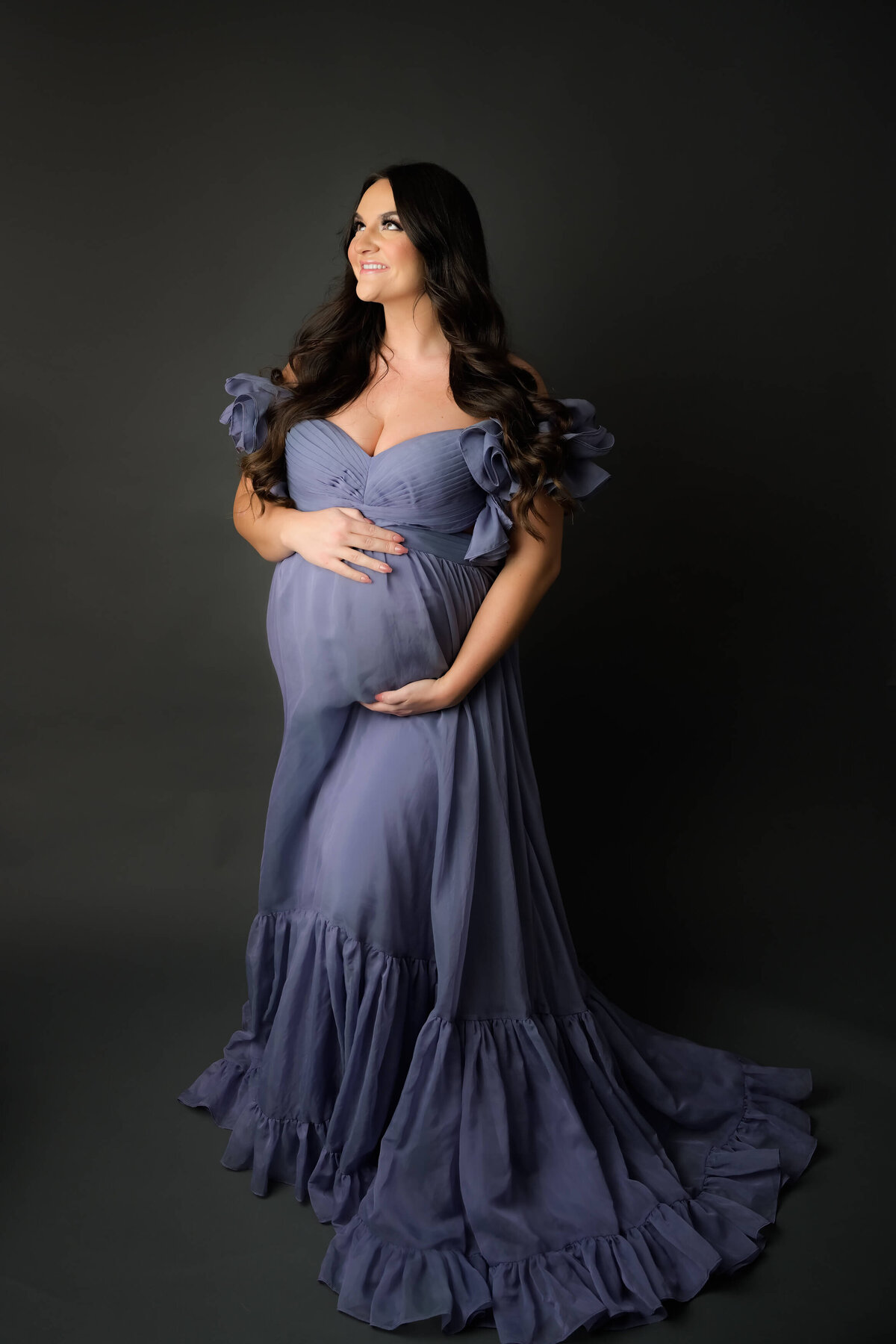 Low key lighting for this maternity photo session.  Mom is wearing a long flowing purple dress as she look up and to the side letting the light highlight her face and baby bump.