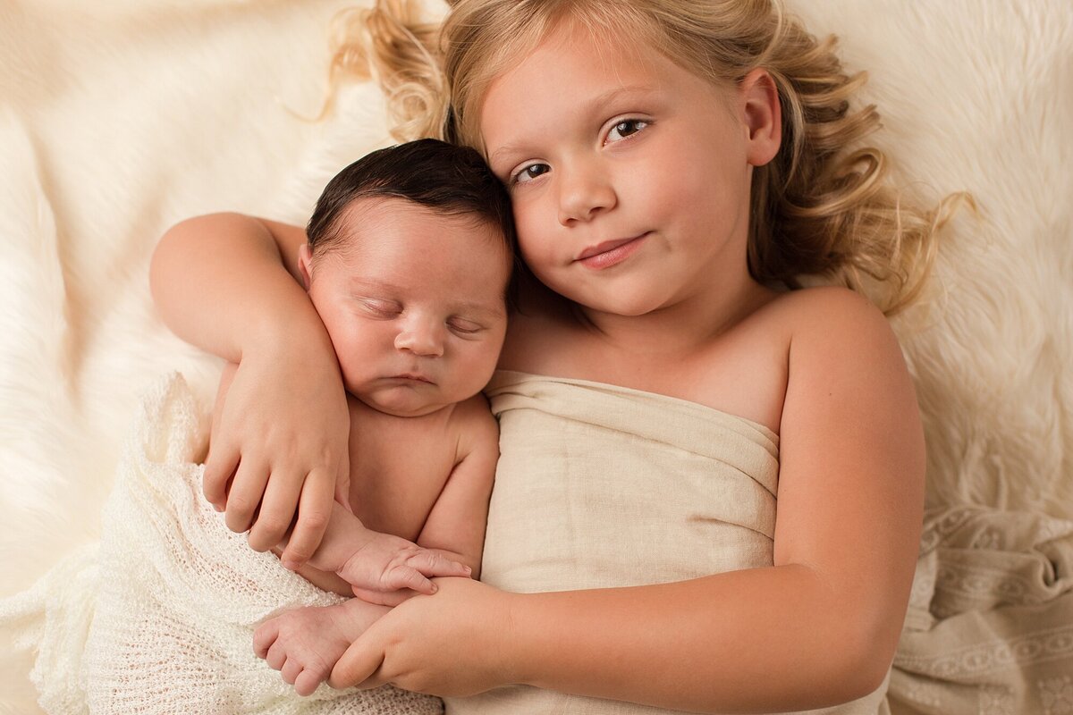 big sister holding baby brother on flokati
