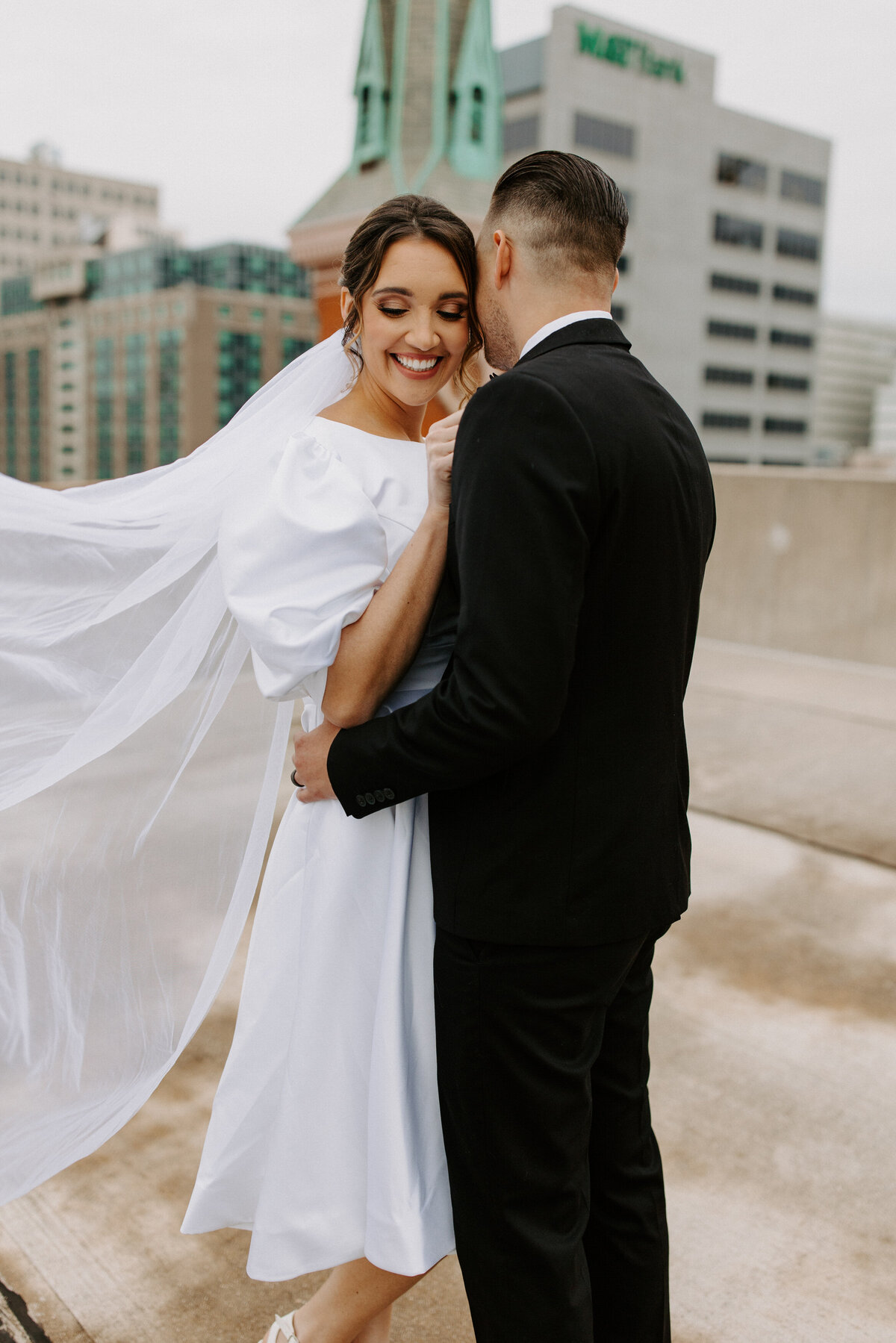 wedding couple hugging each other while on a city rooftop
