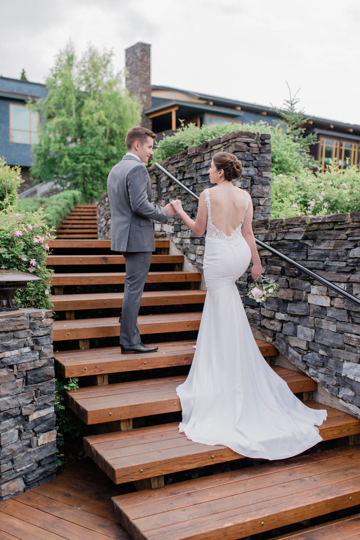 Elegant couple walking up stairs of wedding venue, brides gown trailing on stairs behind her, captured by Kaity Body Photography, elegant film inspired wedding photographer in Calgary, Alberta. Featured on the Bronte Bride Vendor Guide.