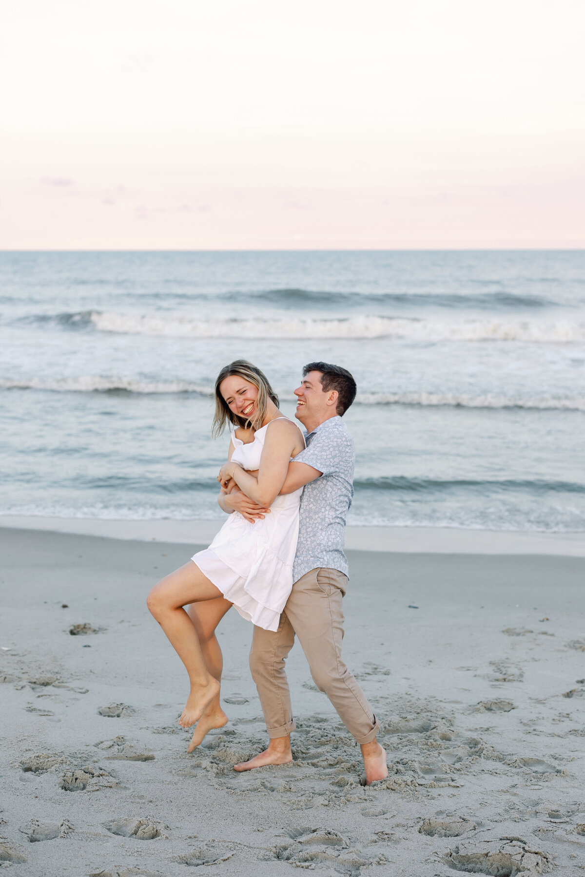 Man catching his fiancée mid-jump on Wilmington beach, dynamic engagement photo