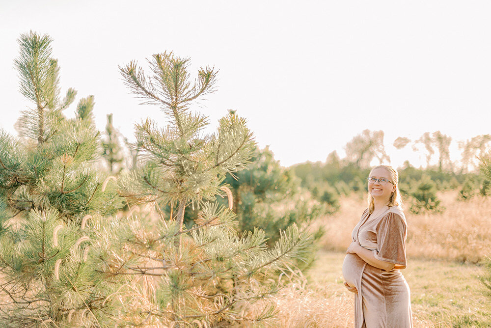 Pregnant person in pink dress at a Christmas tree farm