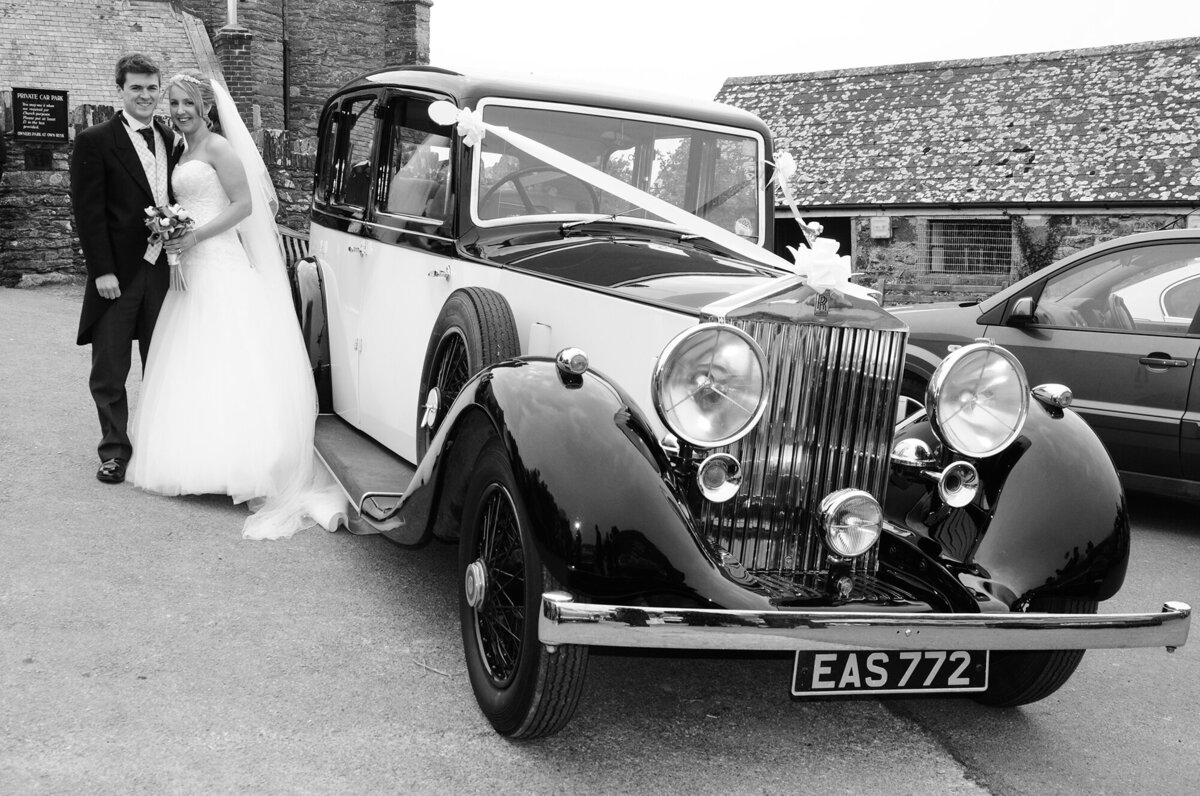 pro-story-photography_bride-and-groom-pose-next-to-vintage-rolls-royce_B&W_wembury-church-plymouth_devon