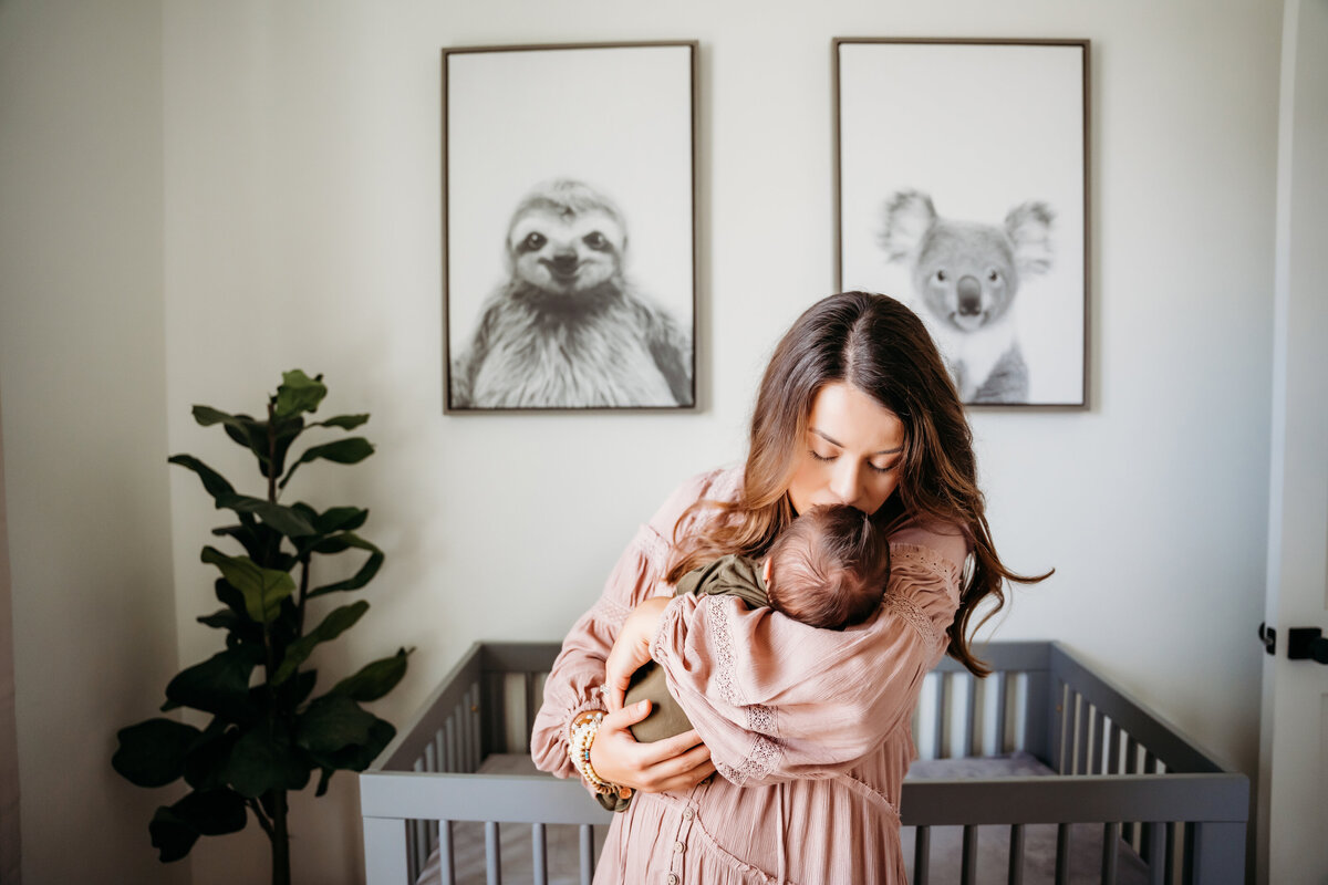 Newborn Photographer, a mother holds her baby and gives her a kiss in the nursery