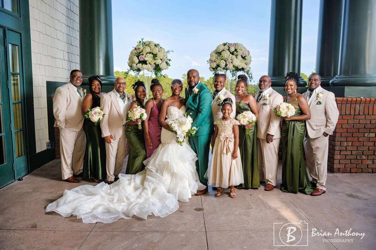 Bride, groom, and wedding party posing for a joyful group portrait at a beautiful venue.
