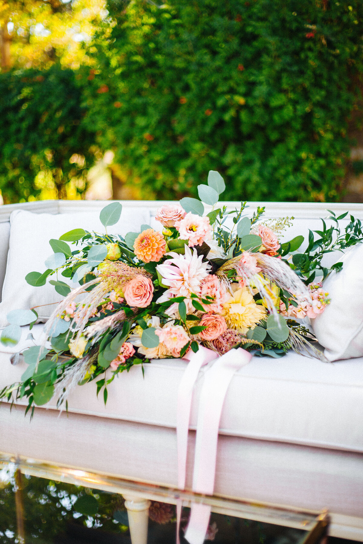 Large boho style bouquet of roses and dahlias with long ribbons on a blush velvet couch