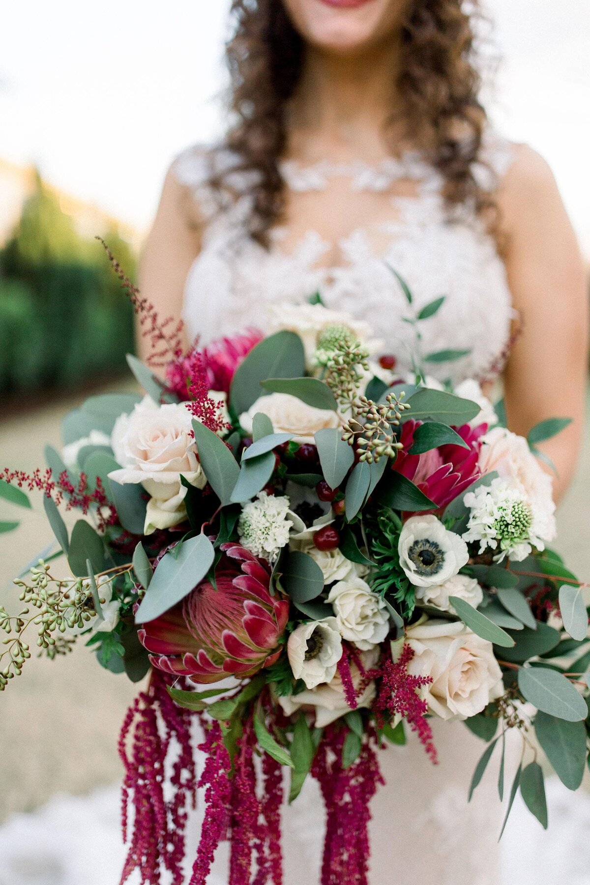 Large bridal bouquet with red protea, anemone, hanging amaranthus, white rose, and mixed eucalyptus greenery