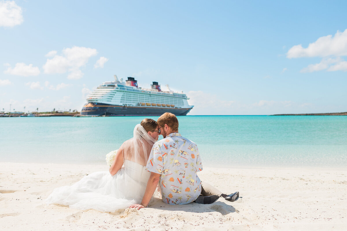 couple sitting on a beach with Disney cruise ship in background