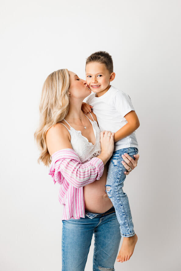 A pregnant mom kisses her son while holding him.