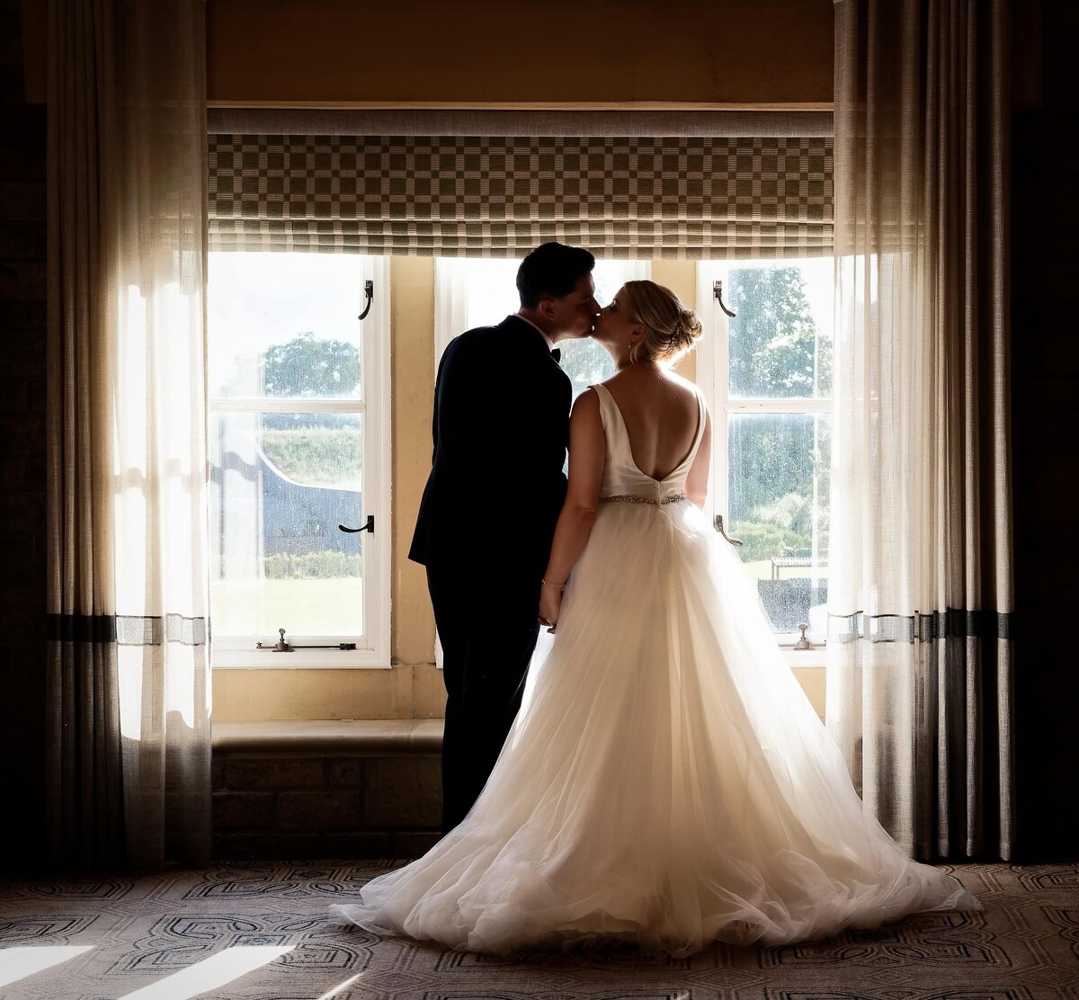 Romantic bride and groom kissing whilst framed by window light at South Lodge. 