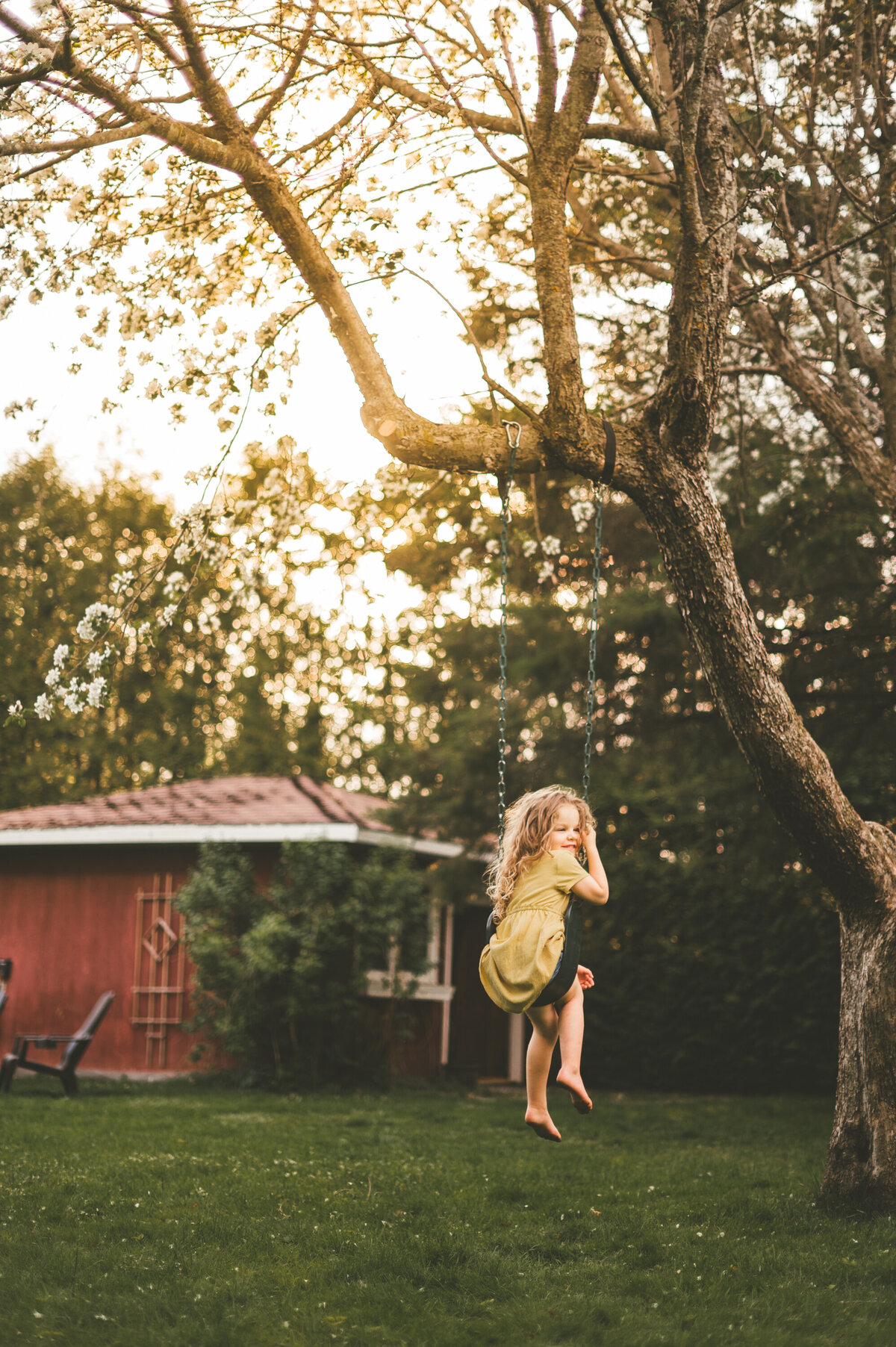 Girl with blond curly hair, sitting barefoot in a swing in a tree.