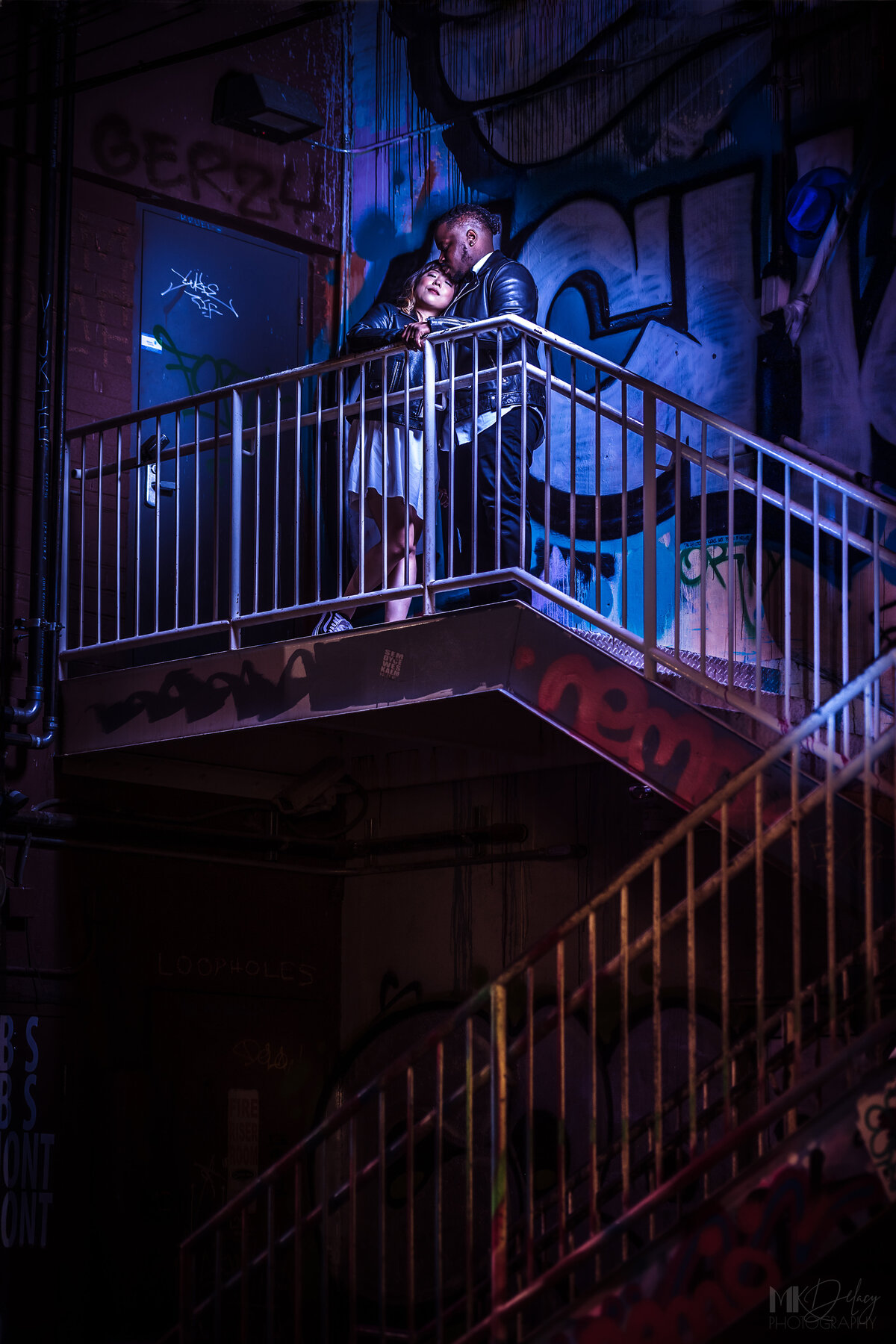 Graffiti staircase romeo and juliet pose bride in white dress with black leather jacket grom in skinny jeans and white dress shirt with black leather jacket wearing  converse on Fremont st  las vegas elopement eloping in vegas  las vegas wedding photographers las vegas wedding photography mk delacy photography
