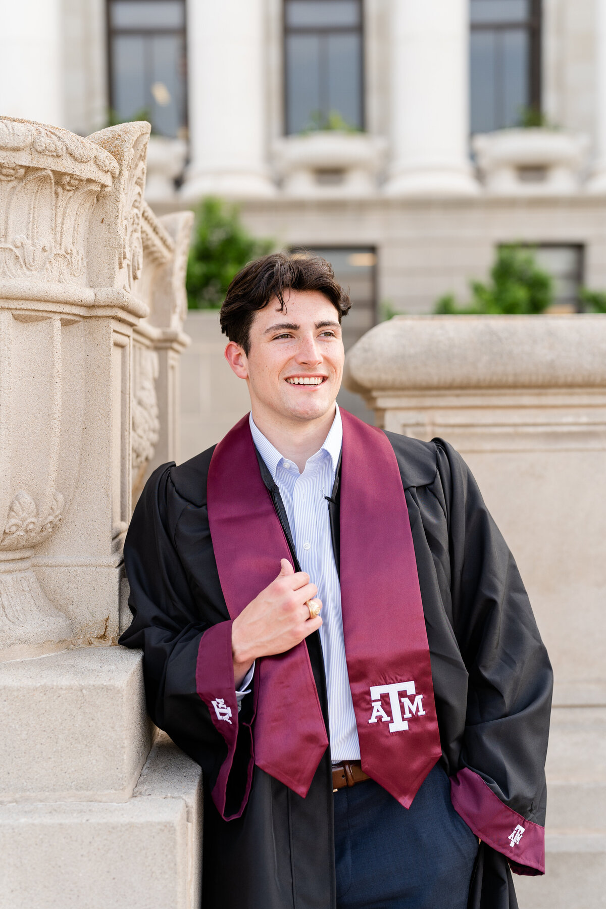 Texas A&M senior guy wearing gown and stole and leaning while smiling away in front of Administration Building